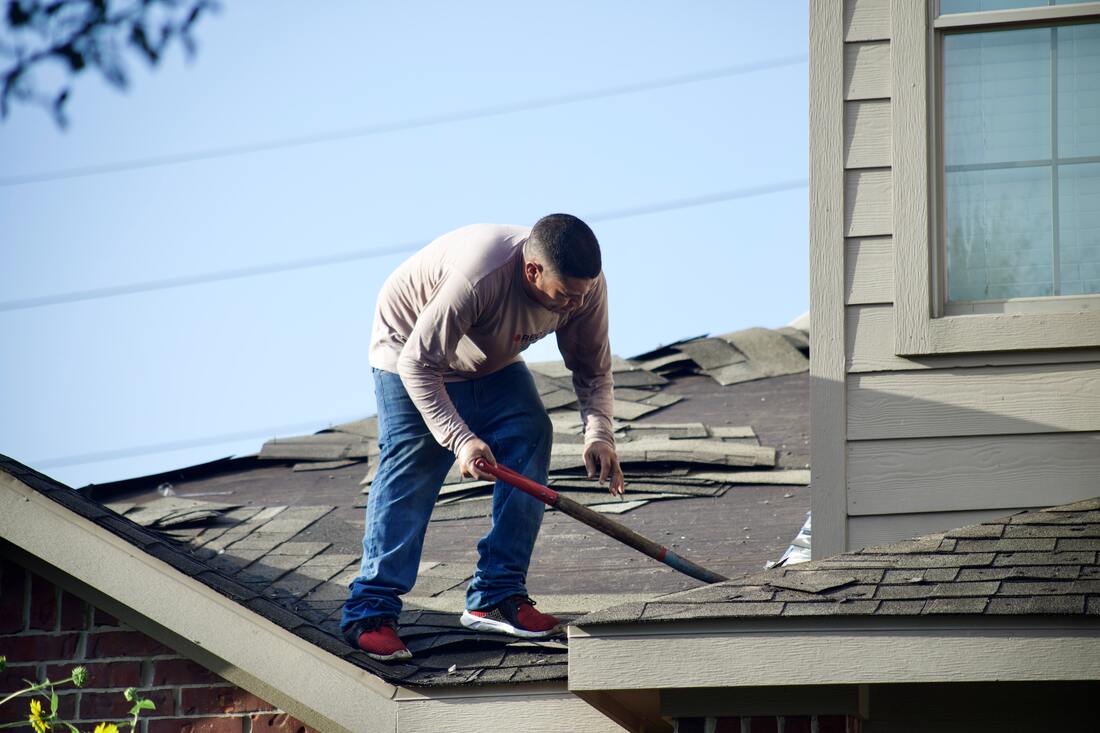 A picture of a man replacing roofing shingles on a house